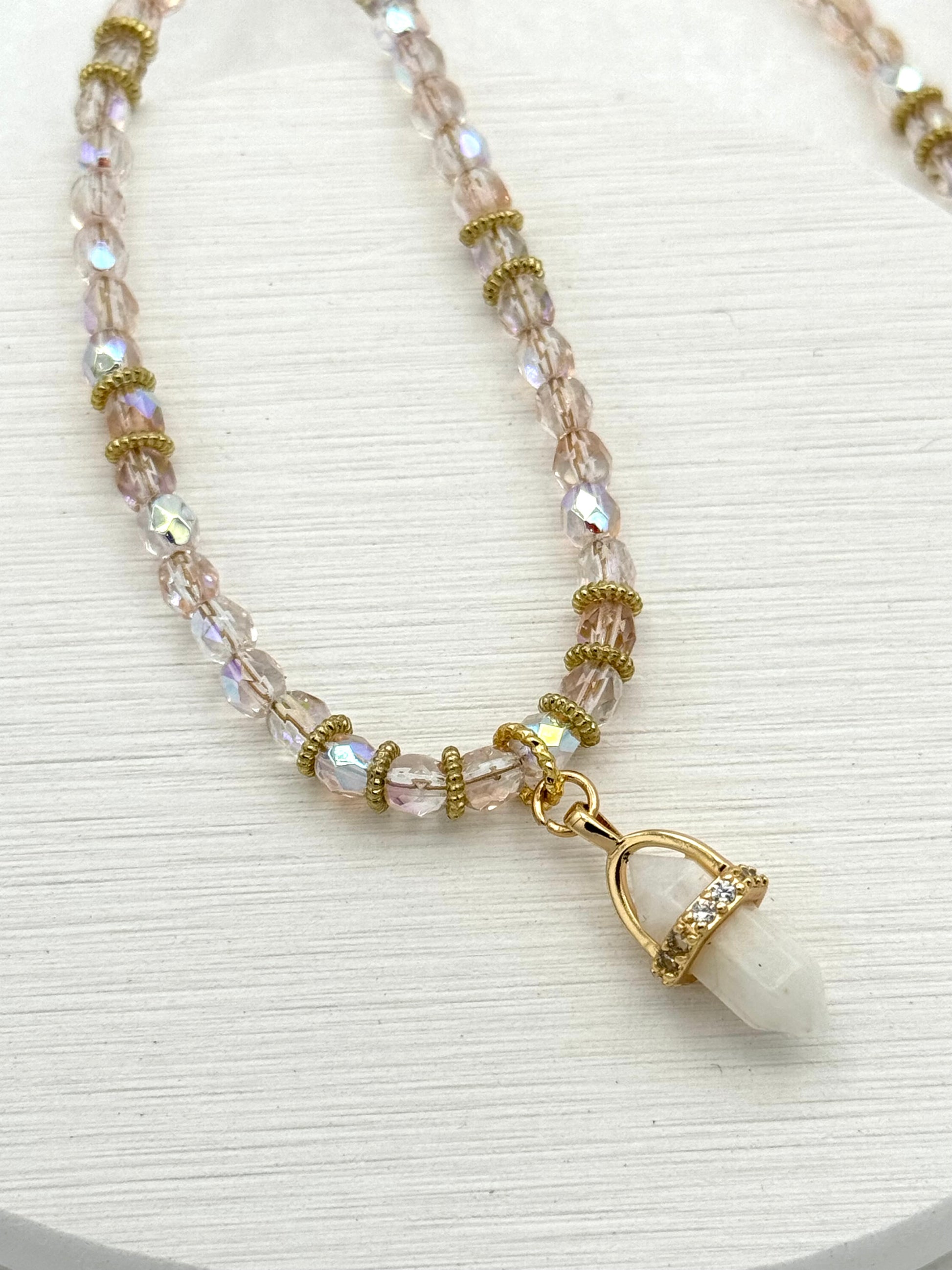 Beaded necklace with a gold clasp and white pendant on a white background