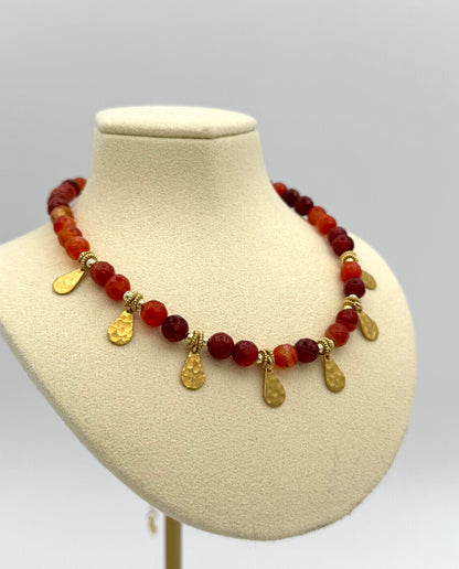Necklace with red beads and gold pendants on a mannequin bust against a gray background