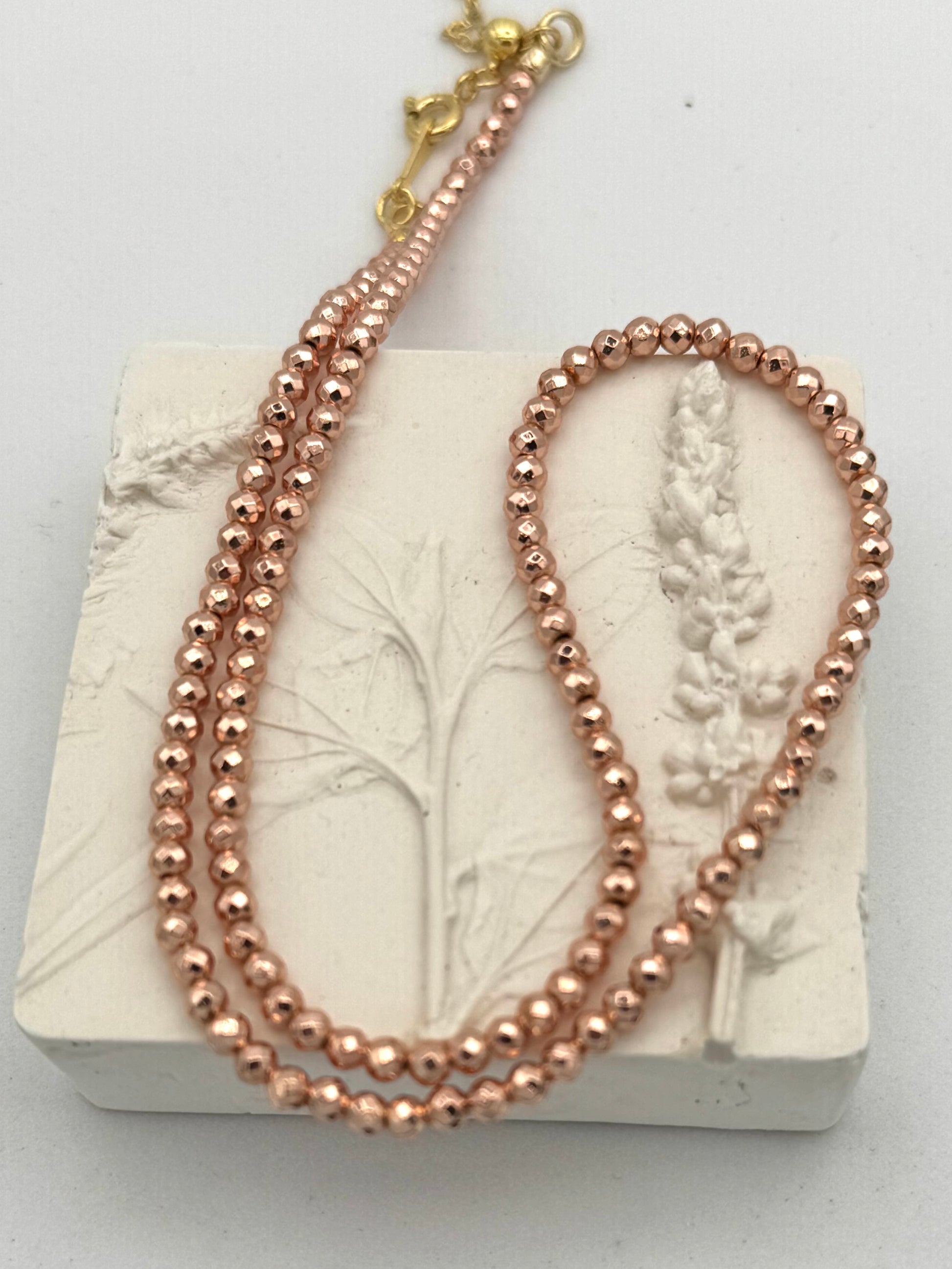 Rose gold beaded necklace on a white stone surface