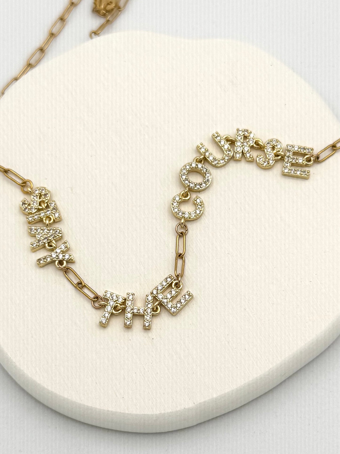 Gold necklace with words Stay The Course on a white surface