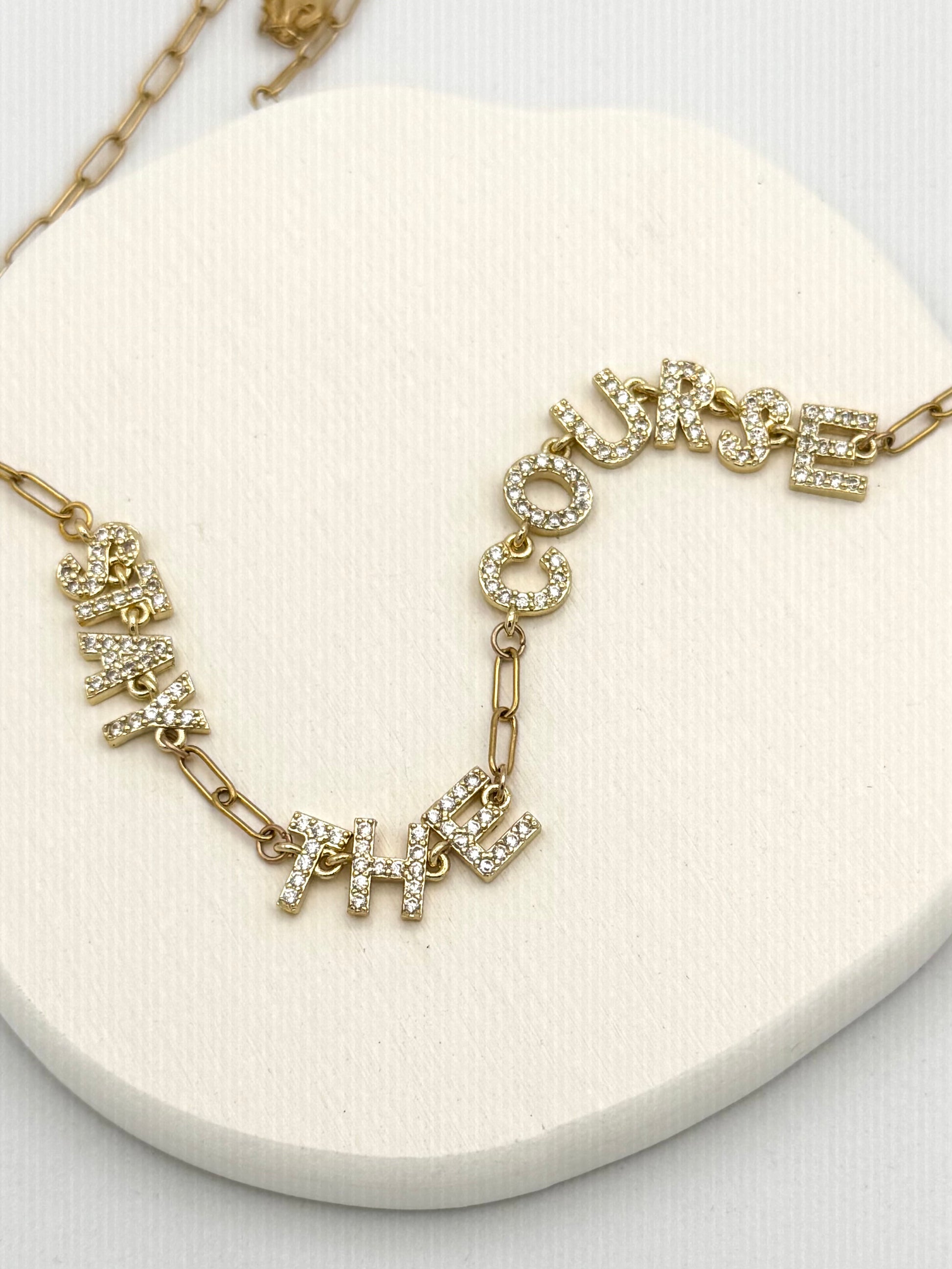 Gold necklace with words Stay The Course on a white surface