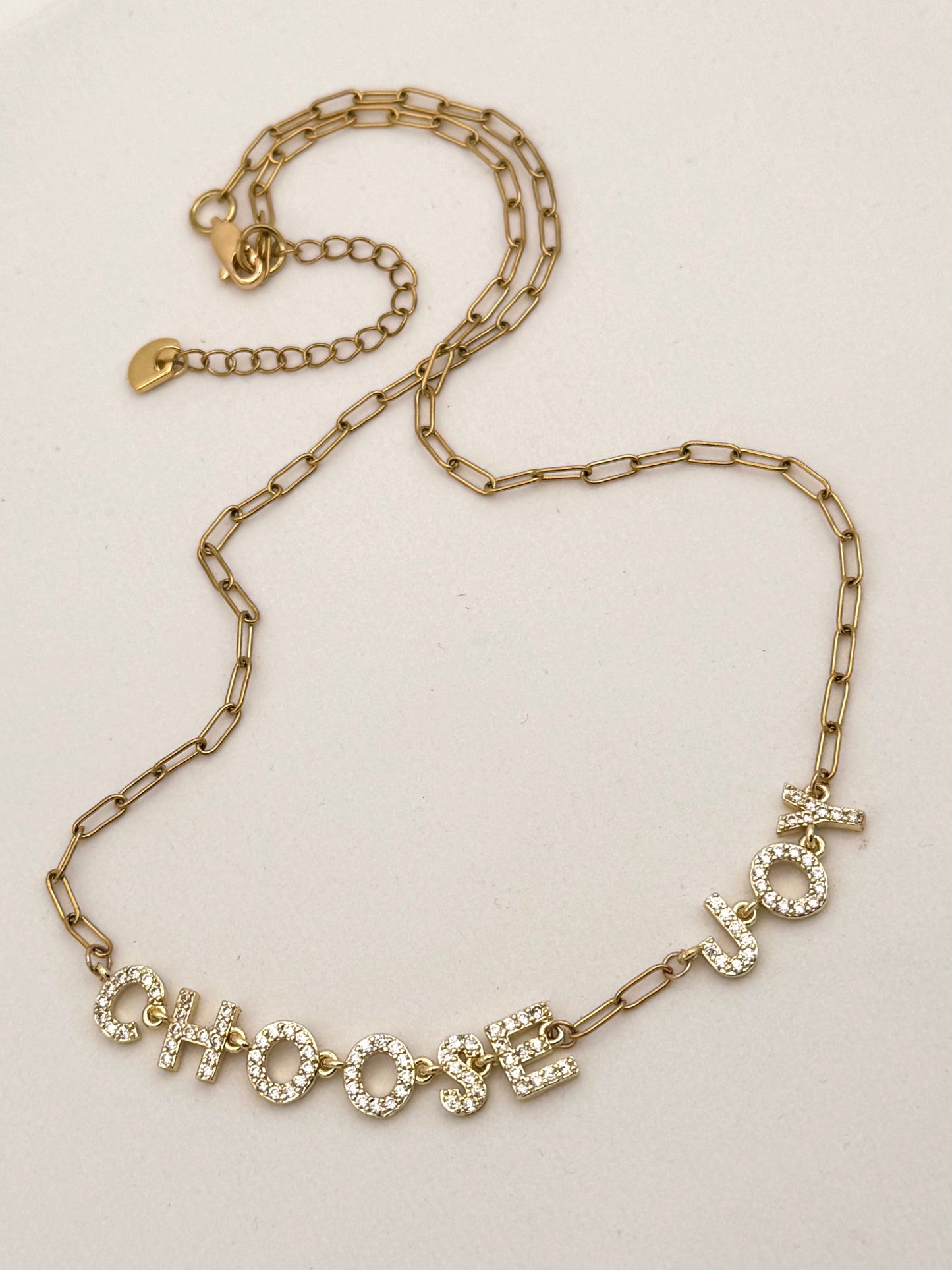 Gold chain necklace with 'CHOOSE JOY' pendant on a light background