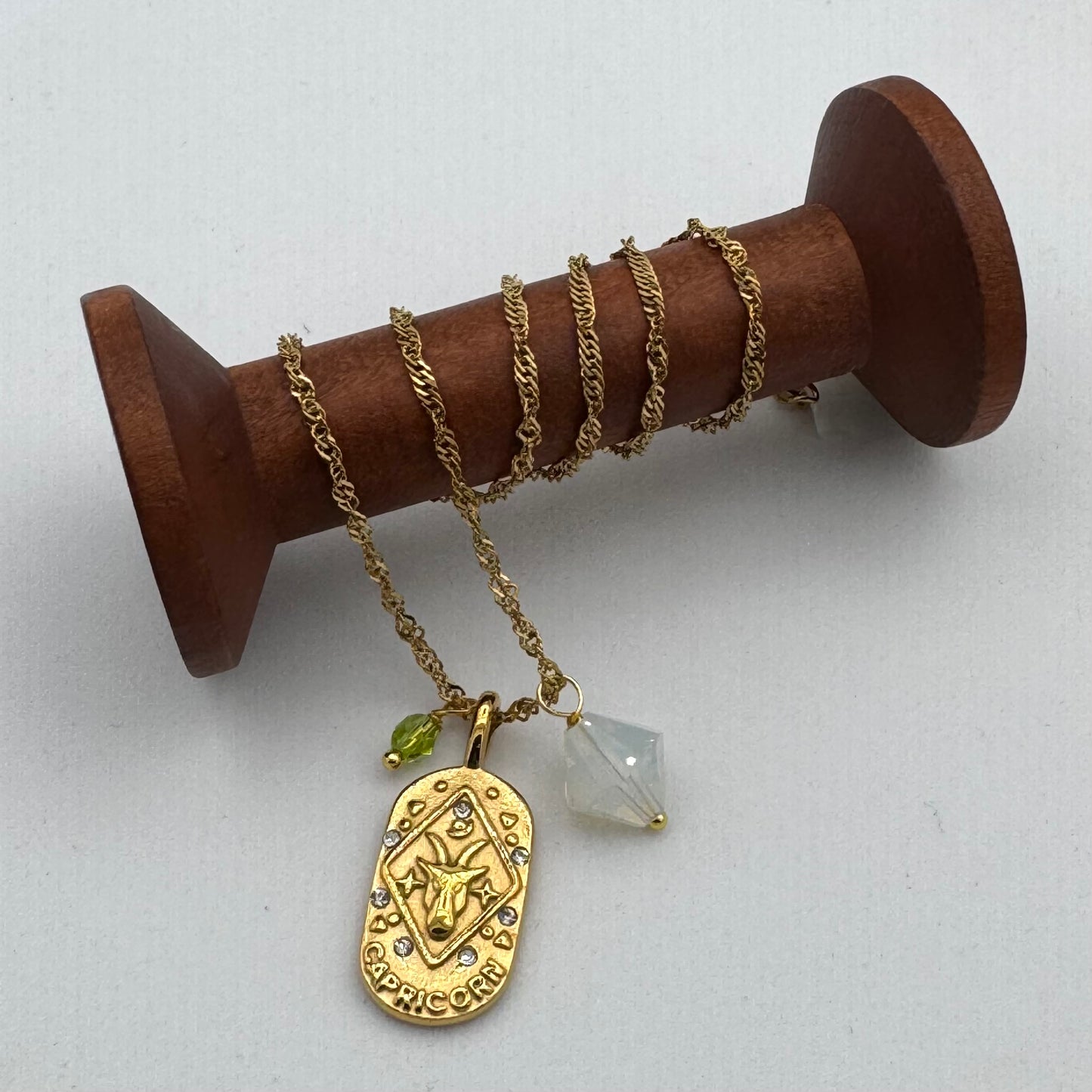 Gold necklace with a pendant and clear crystal on a wooden spool against a light gray background