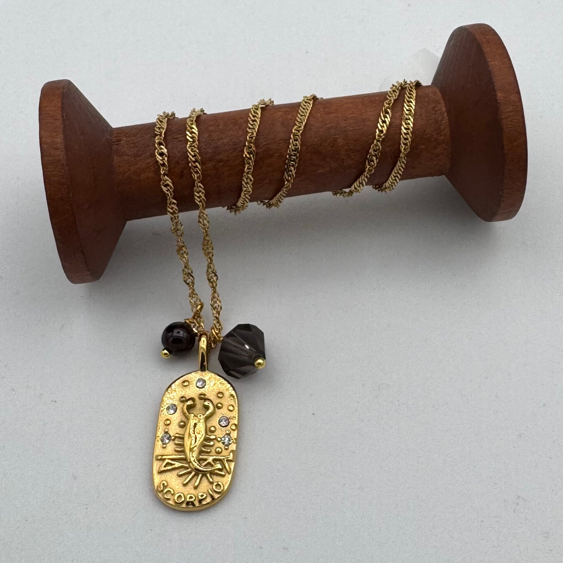 Gold necklace with pendant on a wooden spool against a white background