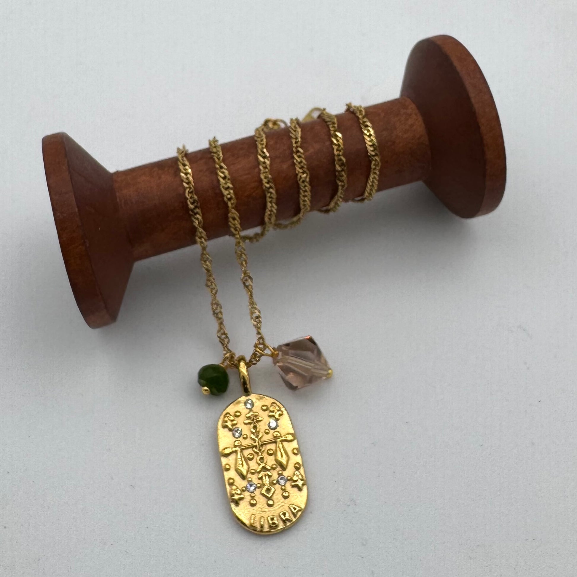 Gold necklace with a pendant on a wooden spool against a white background