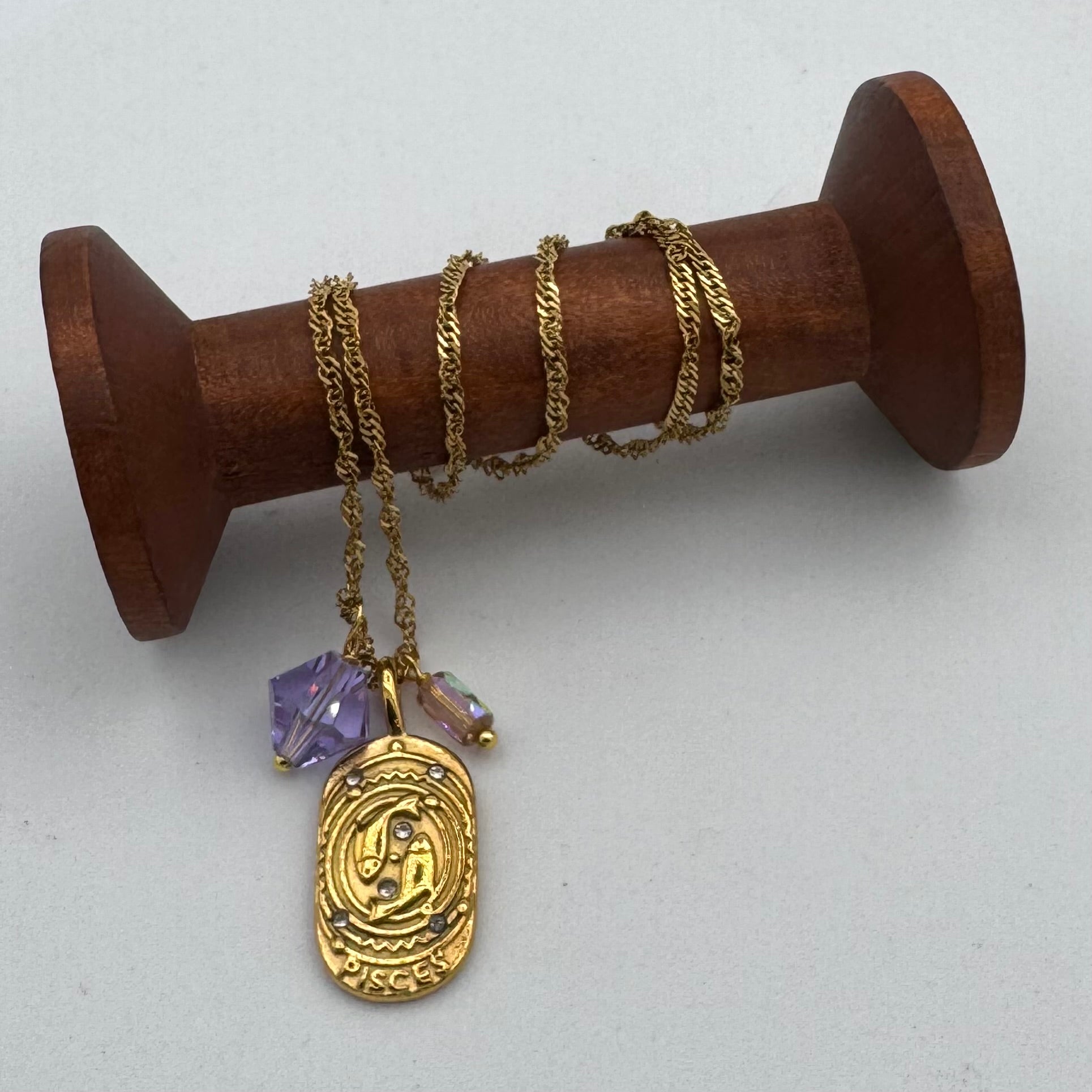 Gold necklace with a purple pendant on a wooden spool against a white background