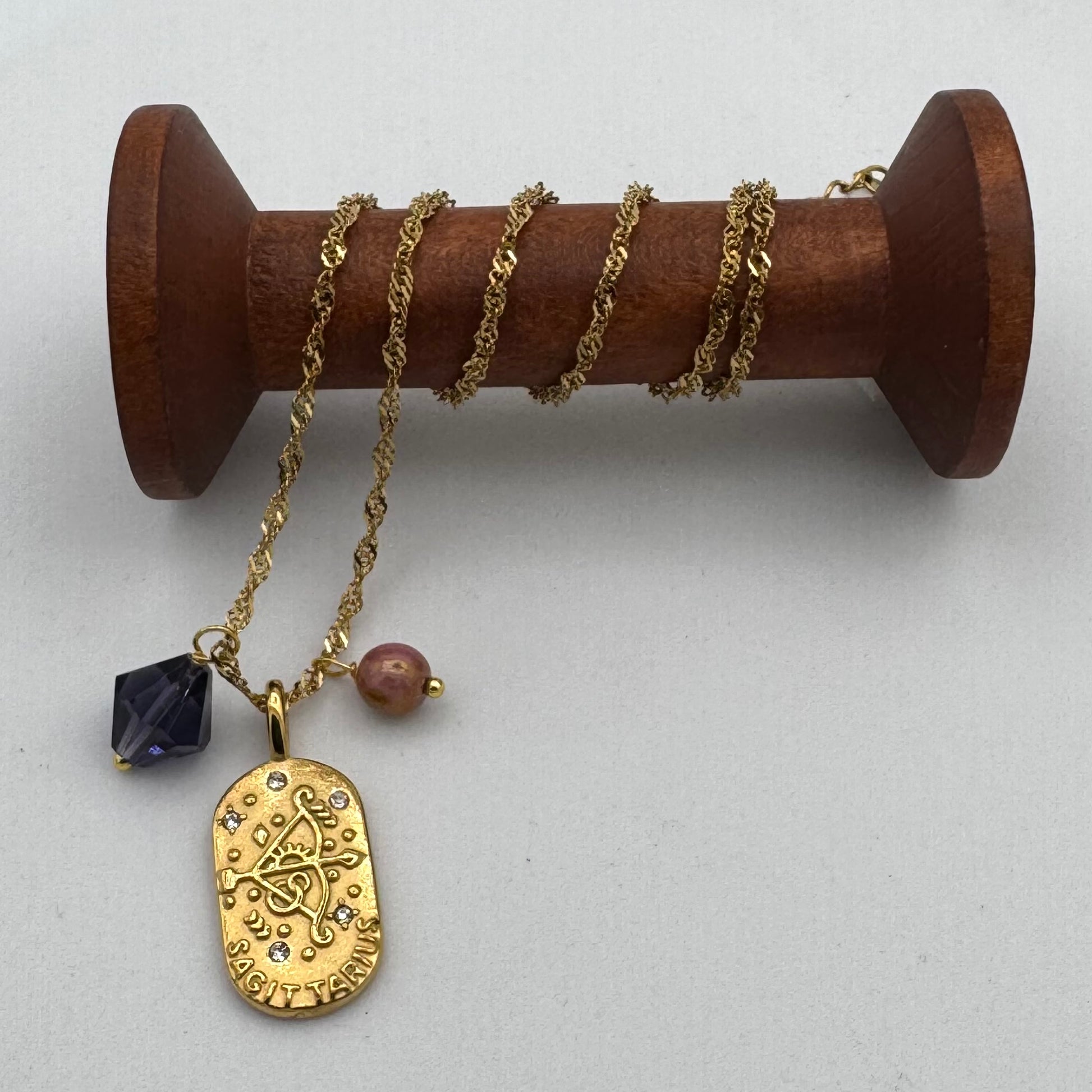 Gold necklace with pendant on a wooden spool against a white background