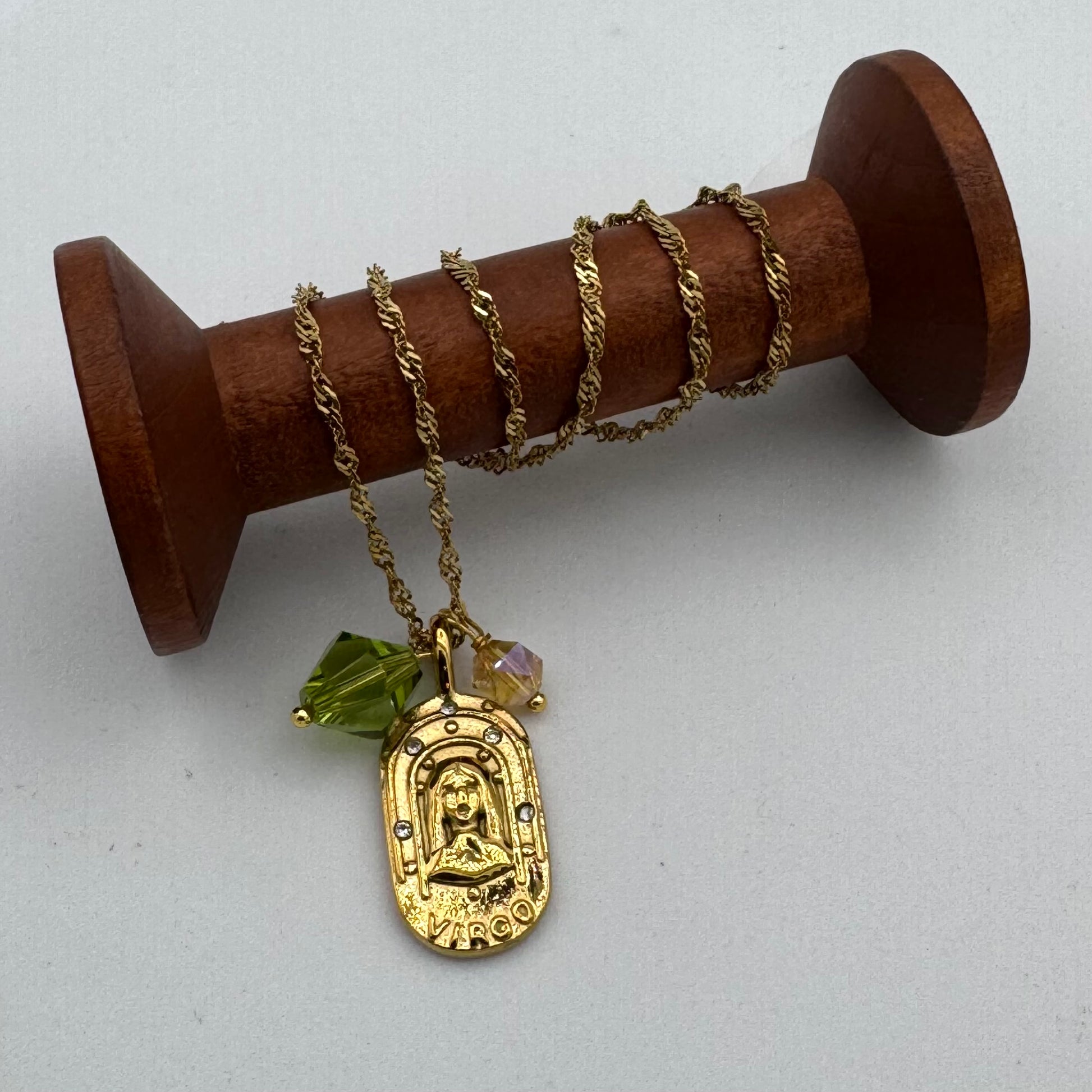 Gold necklace with a pendant on a wooden spool against a white background