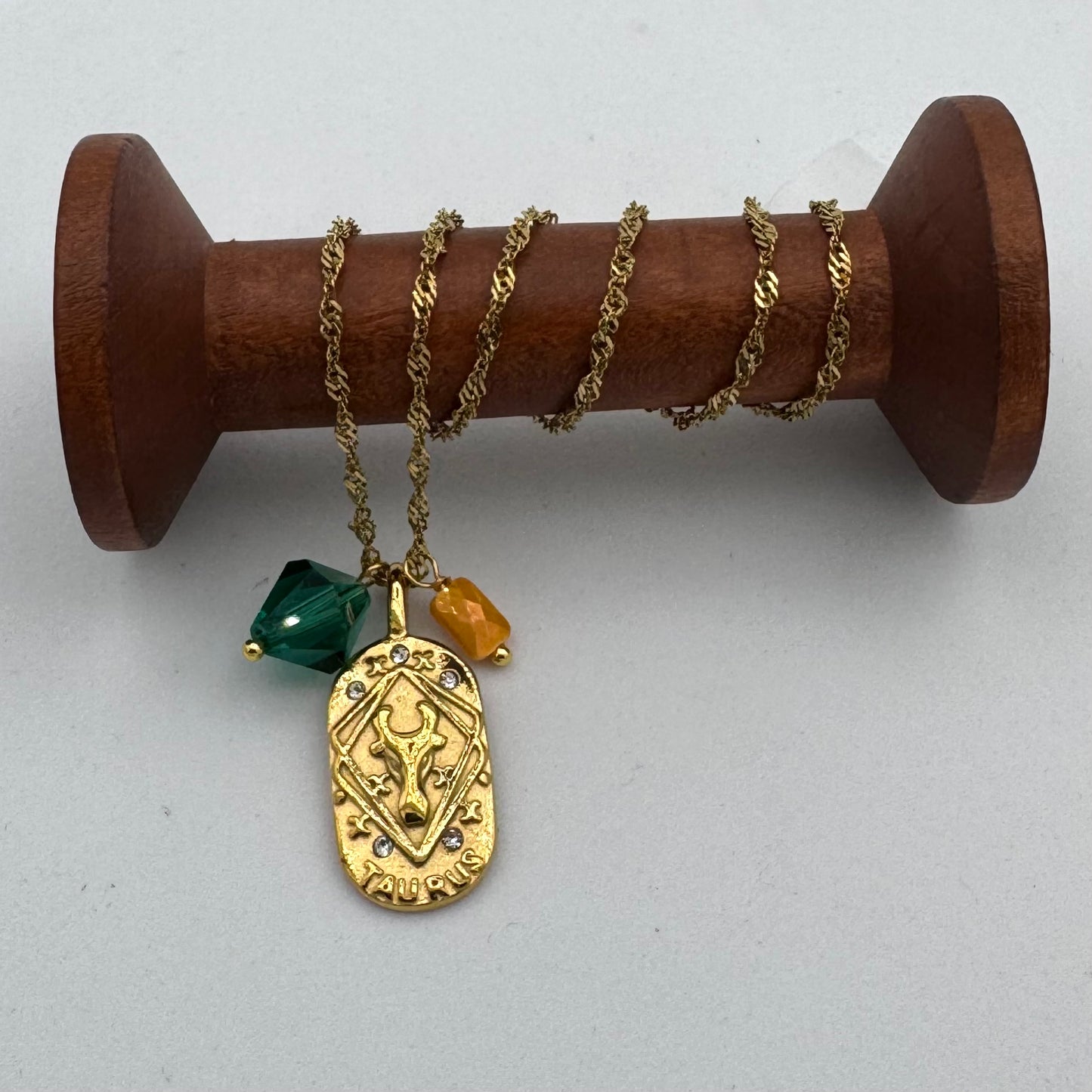 Gold necklace with a pendant and beads on a wooden spool against a white background