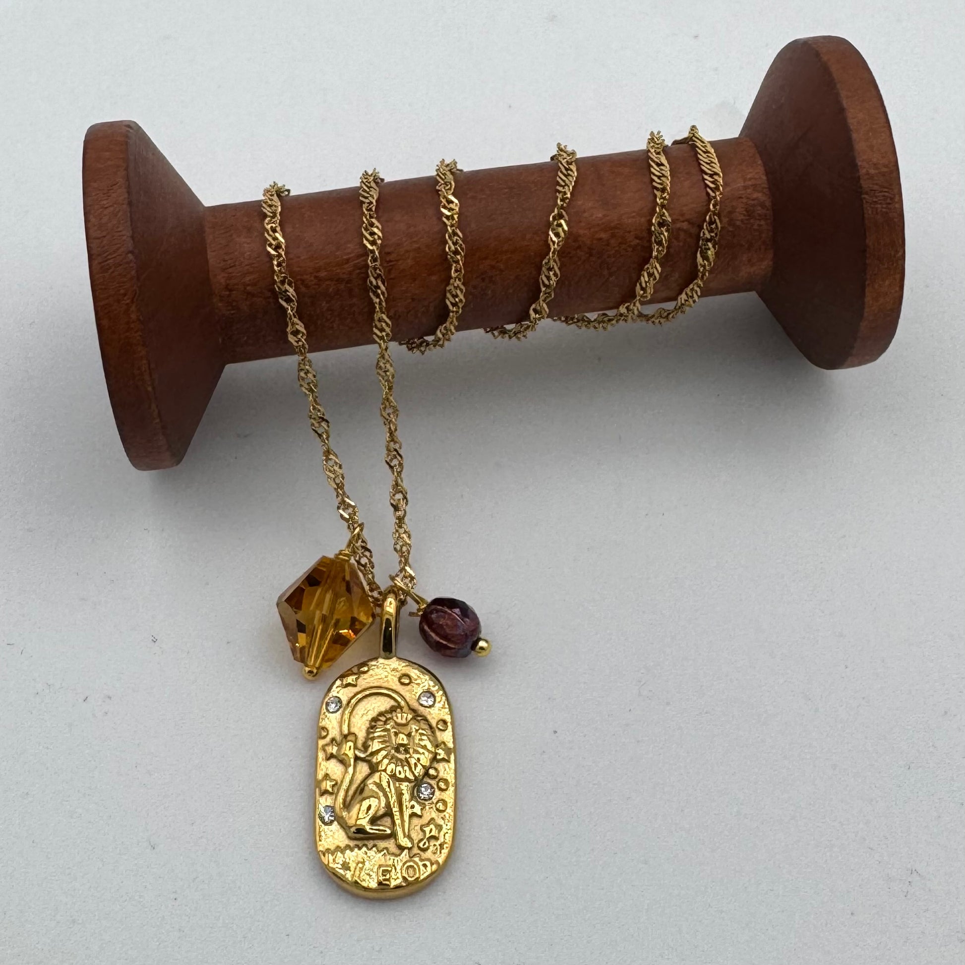 Gold necklace with a pendant on a wooden spool against a white background