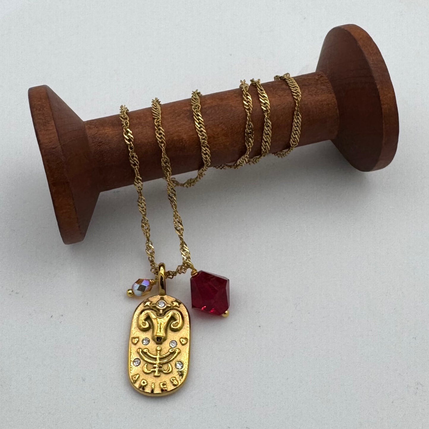 Gold necklace with a pendant and red gemstone on a wooden spool against a white background