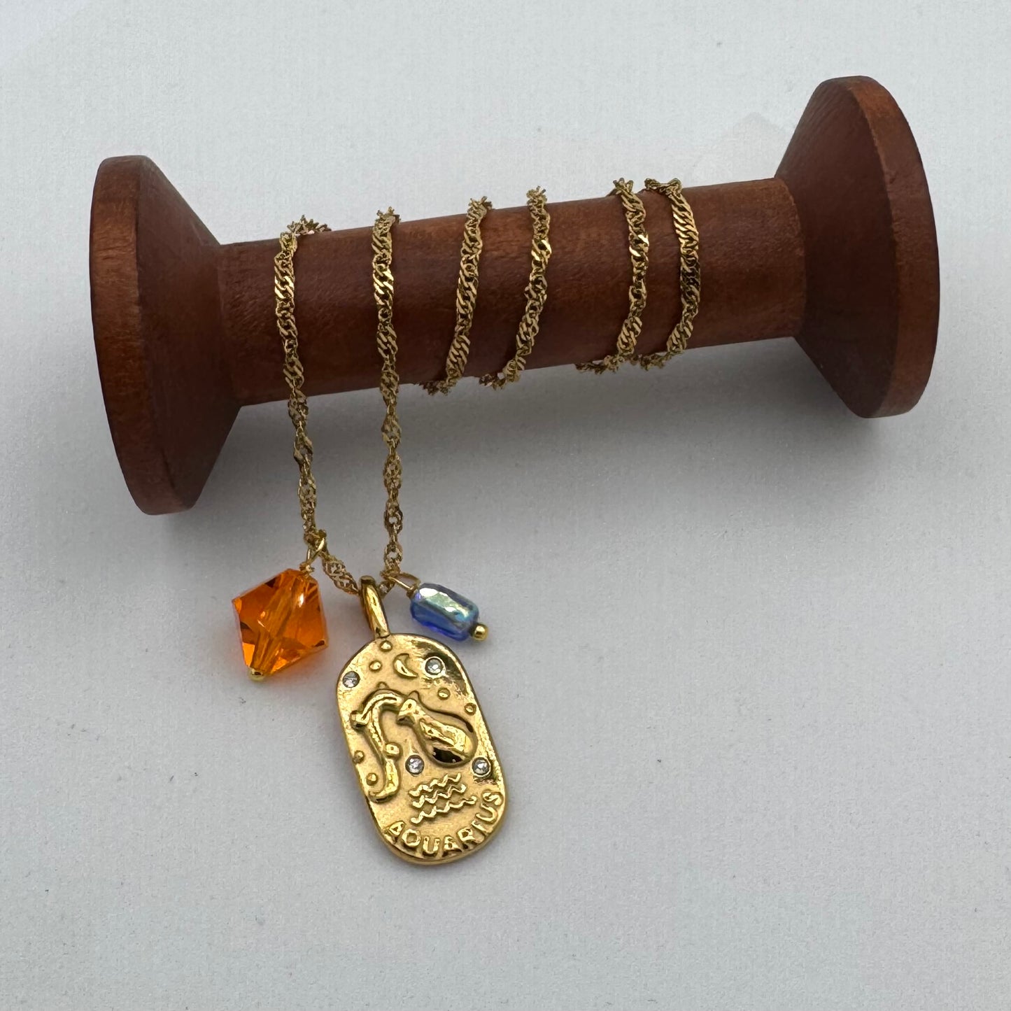 Gold necklace with a pendant and beads on a wooden spool against a white background
