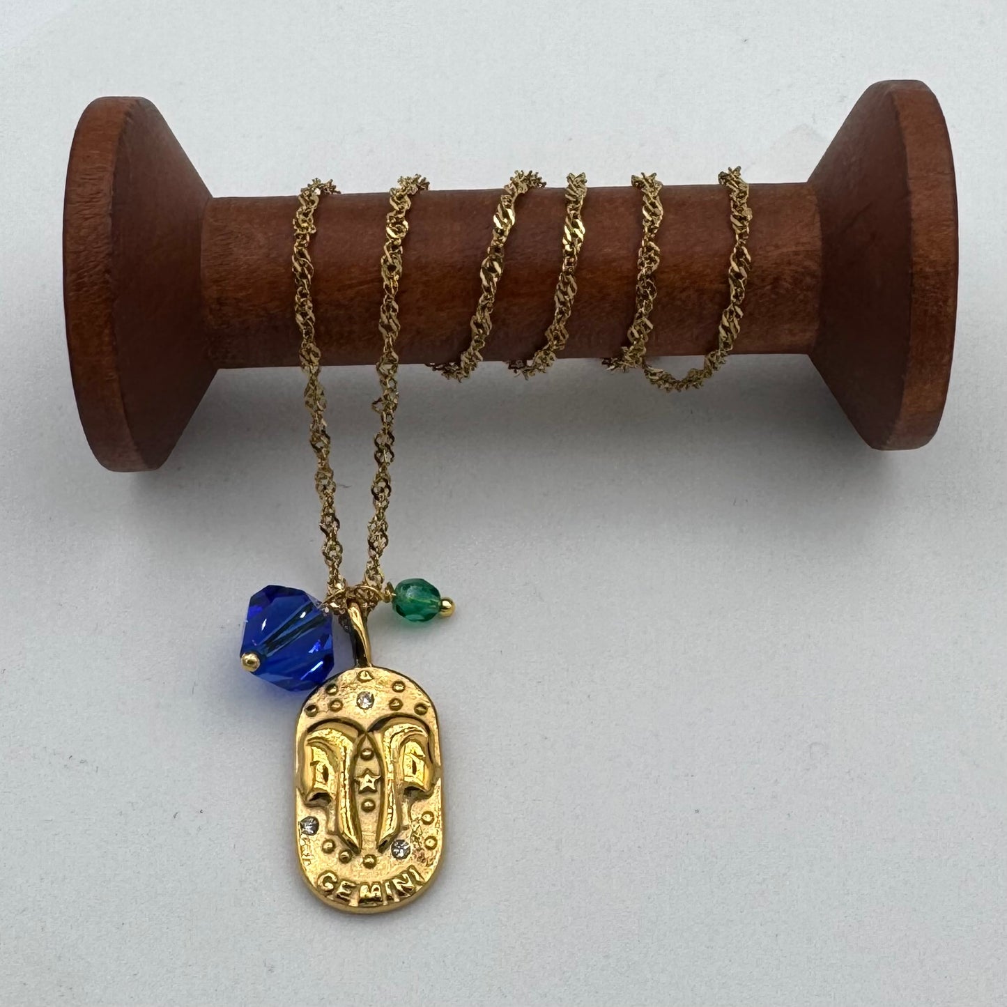 Gold necklace with a pendant and beads on a wooden spool against a white background