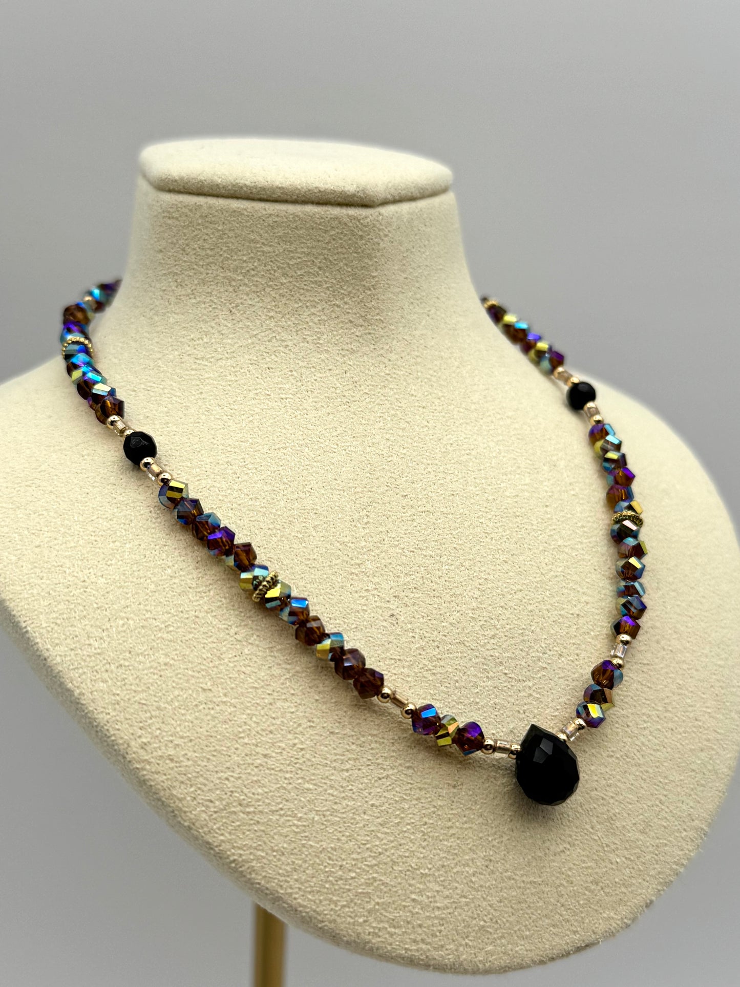 Beaded necklace with black pendant on a mannequin bust against a gray background