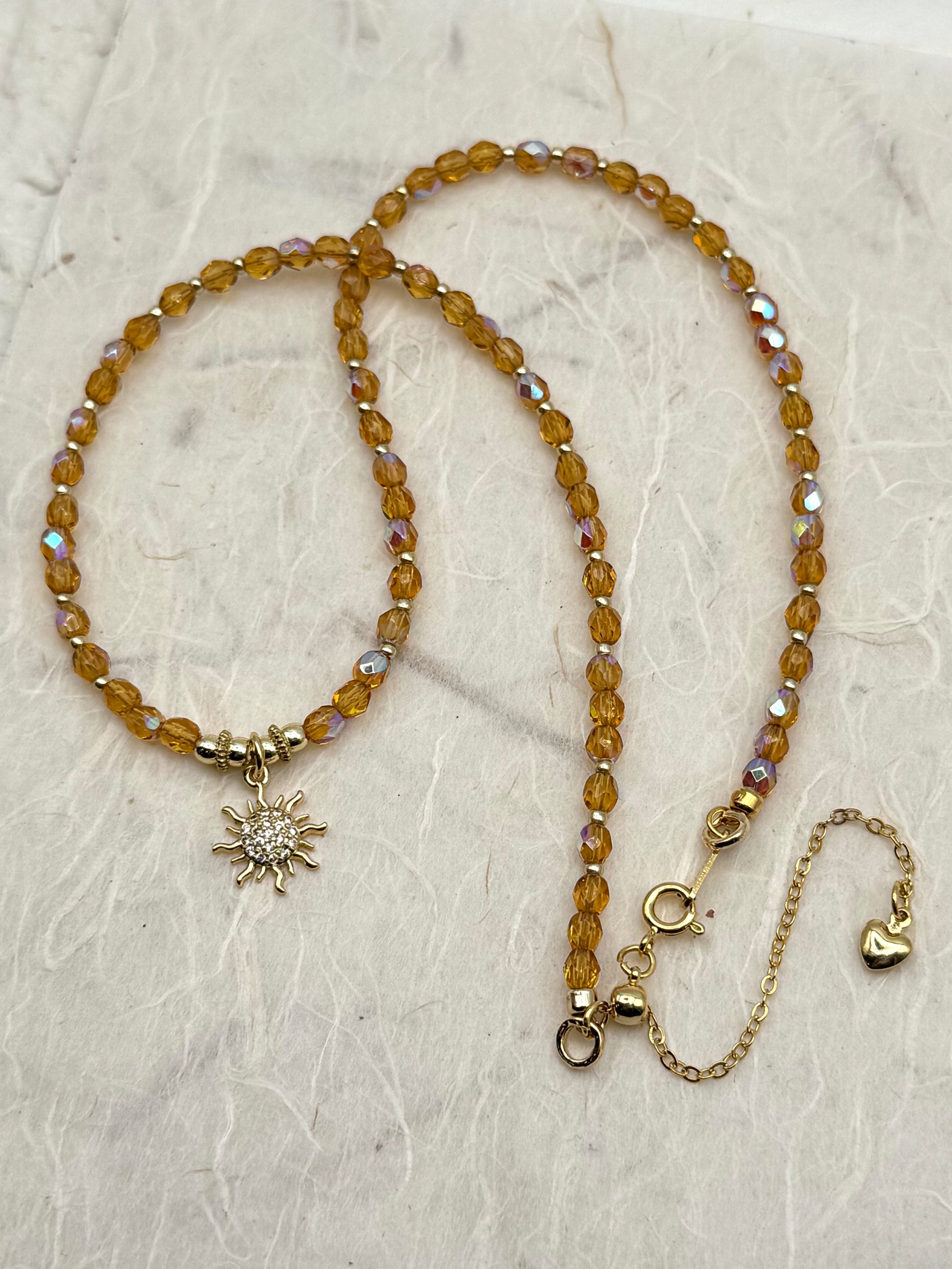 Beaded necklace with sun and heart charms on a textured surface