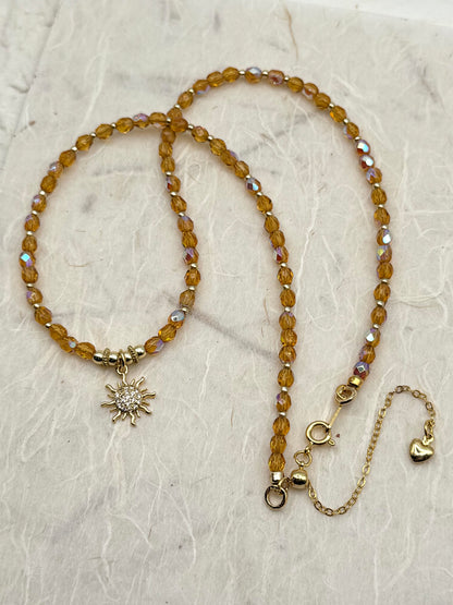 Beaded necklace with sun and heart charms on a textured surface