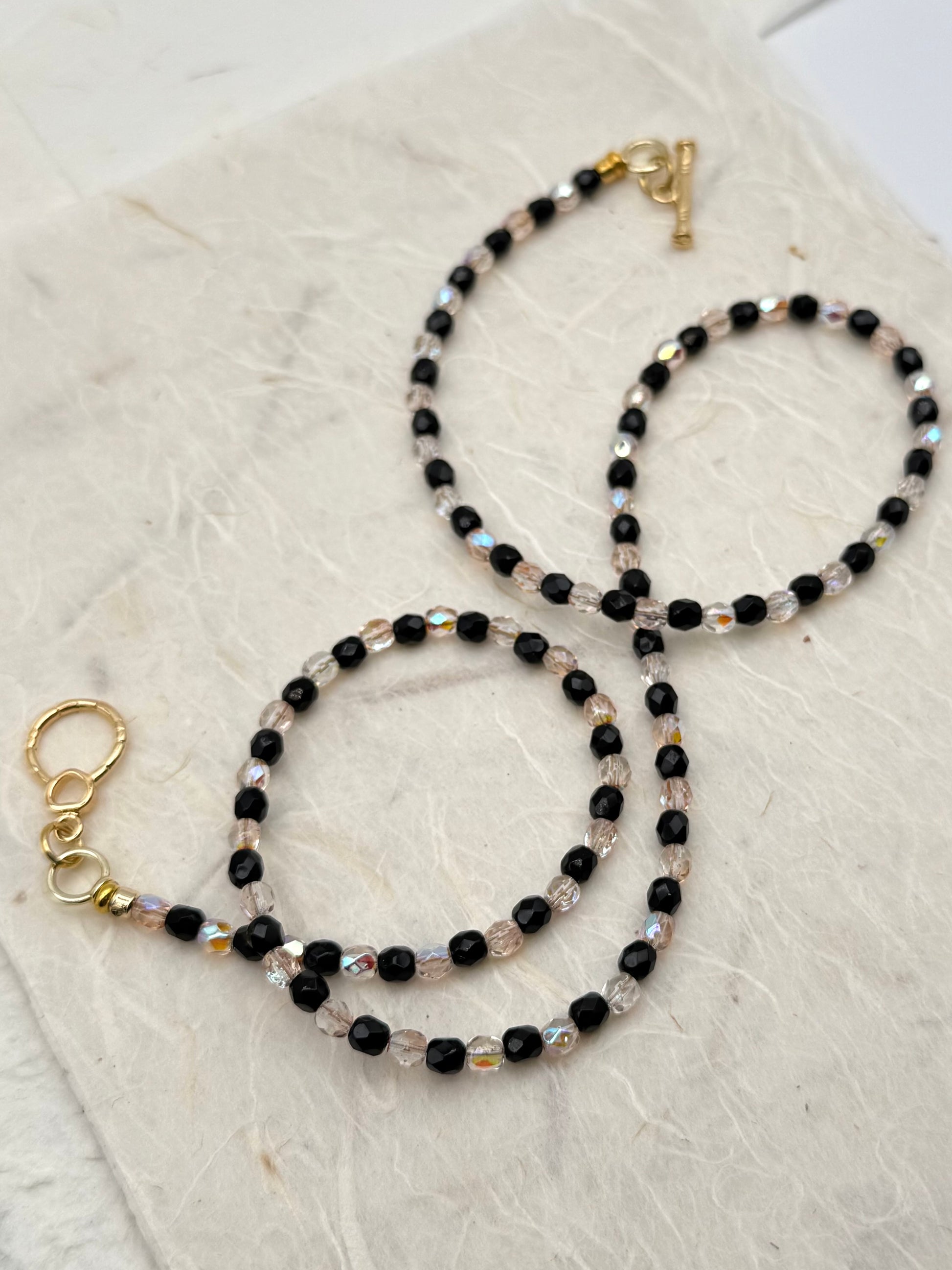 Two beaded necklaces with gold clasps on a textured beige surface