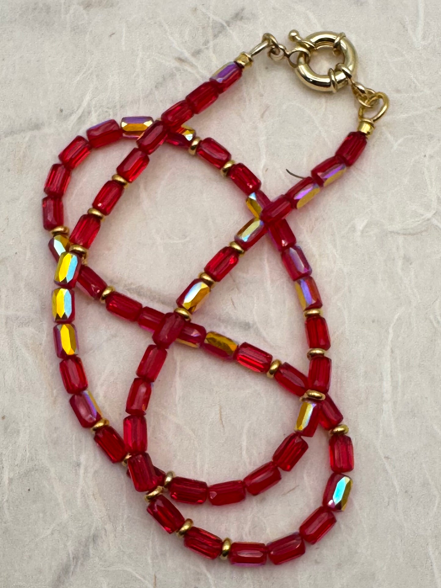 Beaded necklace with red and gold beads on a textured beige background