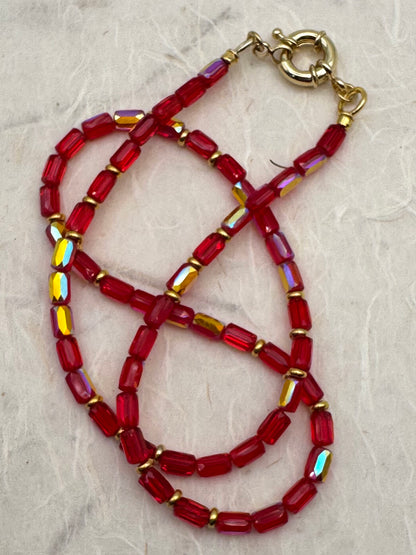 Beaded necklace with red and gold beads on a textured beige background