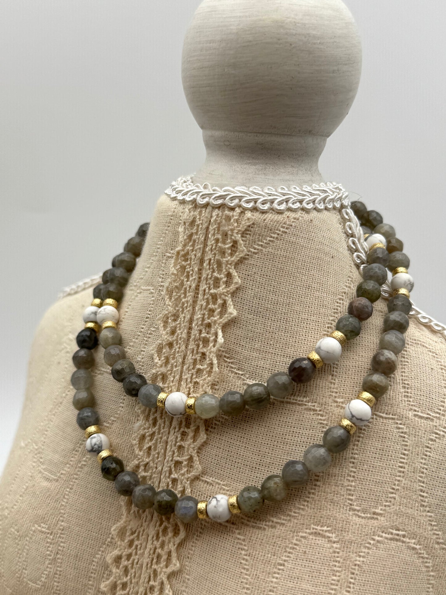 Necklace with beads on a mannequin wearing a textured garment.