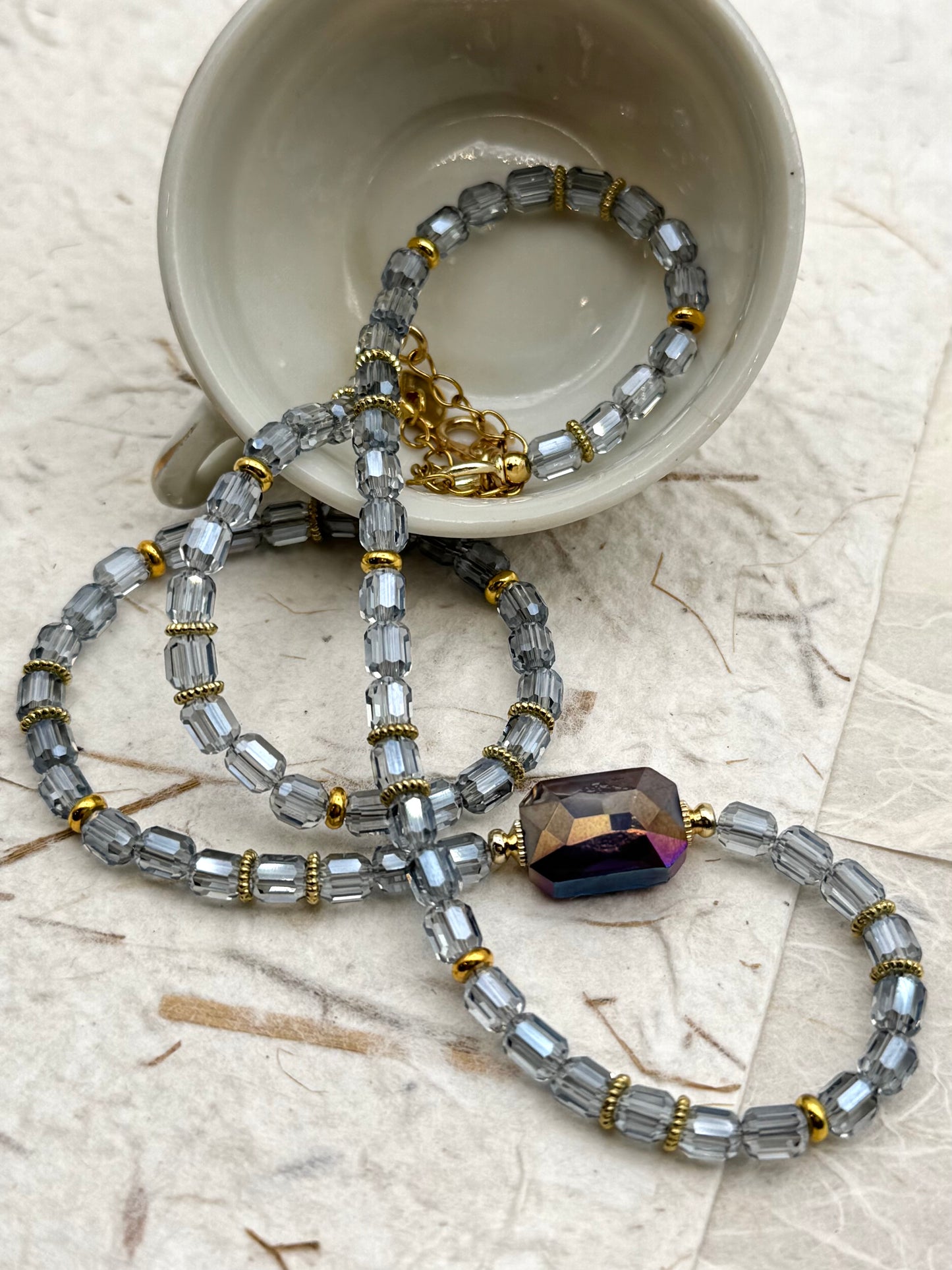 Beaded necklace with a large purple bead on a textured surface with a cup in the background.