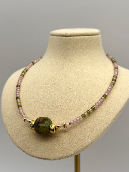 Necklace with green and pink beads on a mannequin bust against a gray background