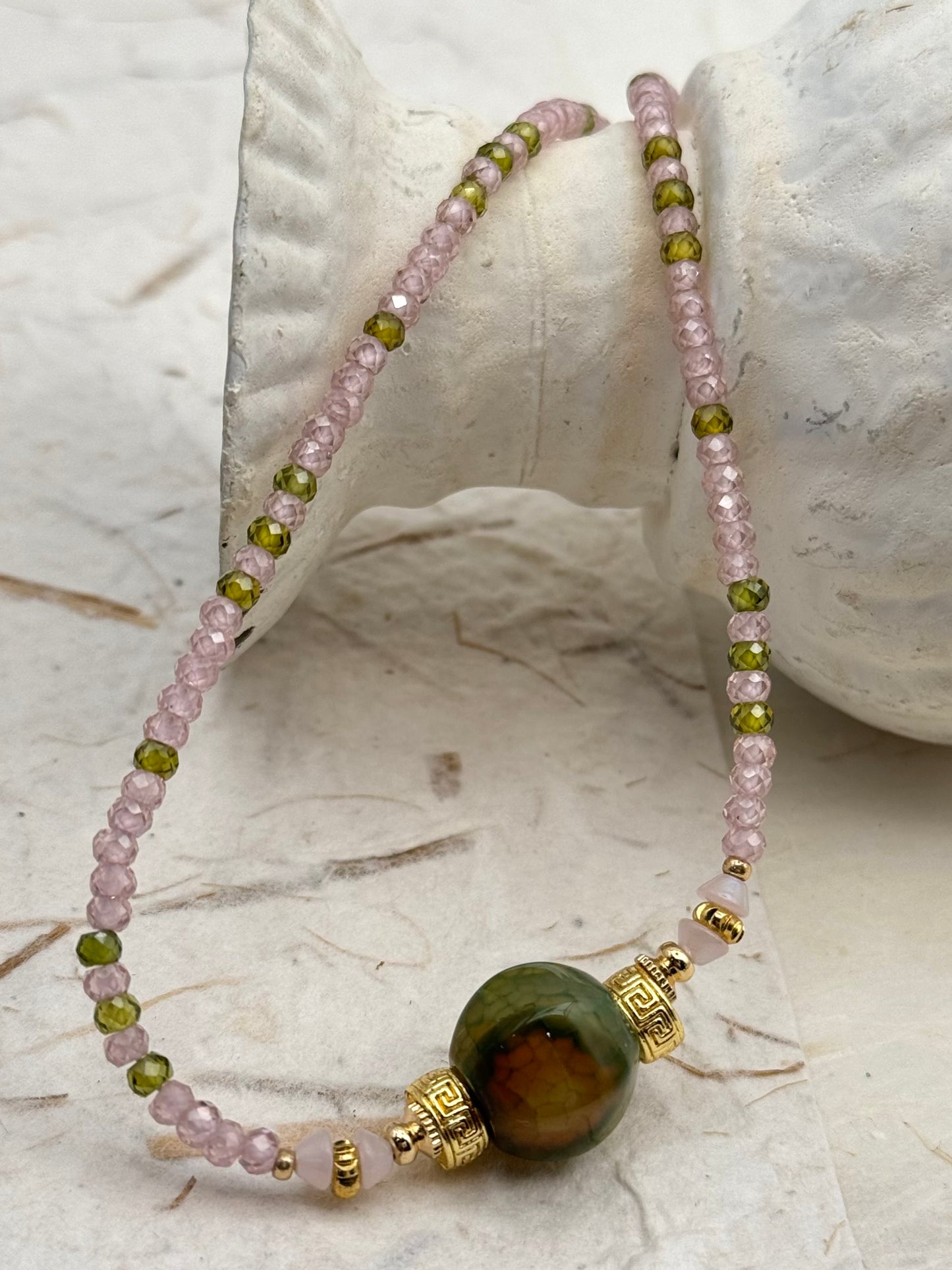 Beaded necklace with green and pink beads on a white shell background