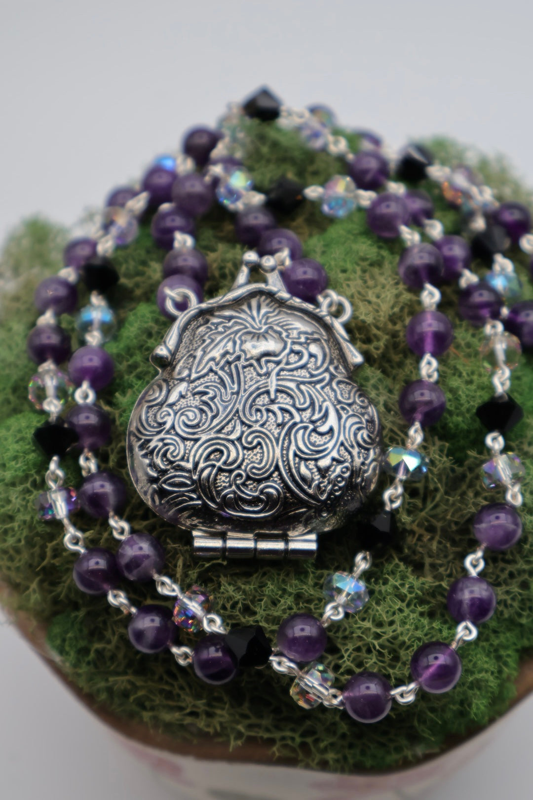 Purple beaded necklace with a silver pendant on a green surface