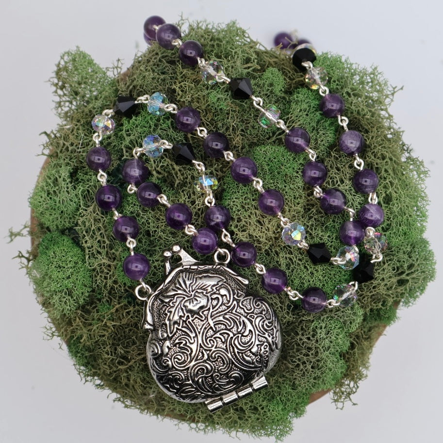 Necklace with purple beads and a silver pendant on a bed of green moss.
