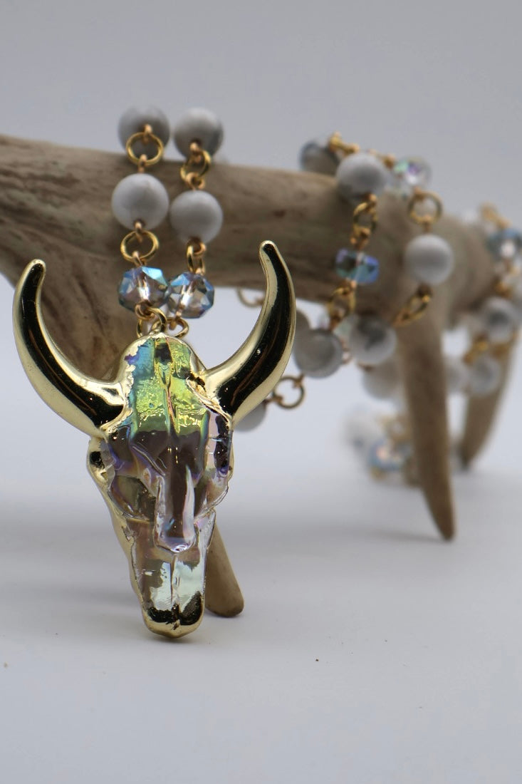 Decorative deer skull with gold horns and beaded necklace on a white background
