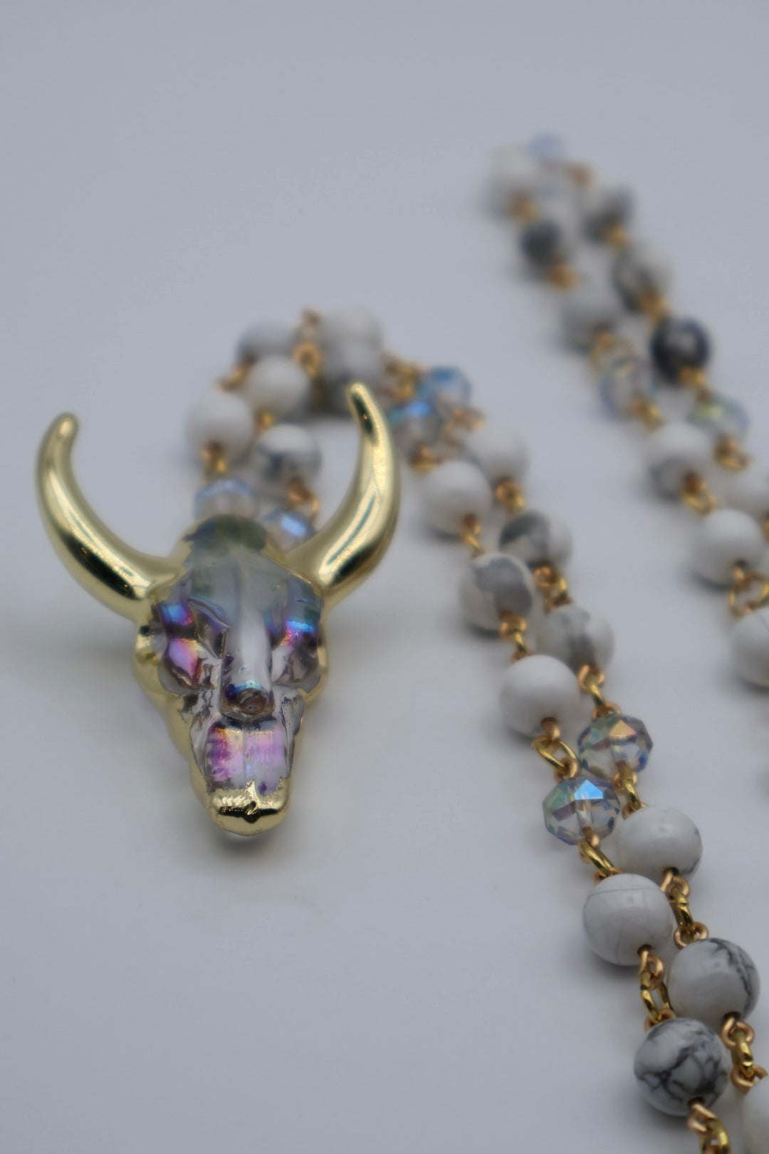 Necklace with a bull skull pendant and white beads on a light gray background