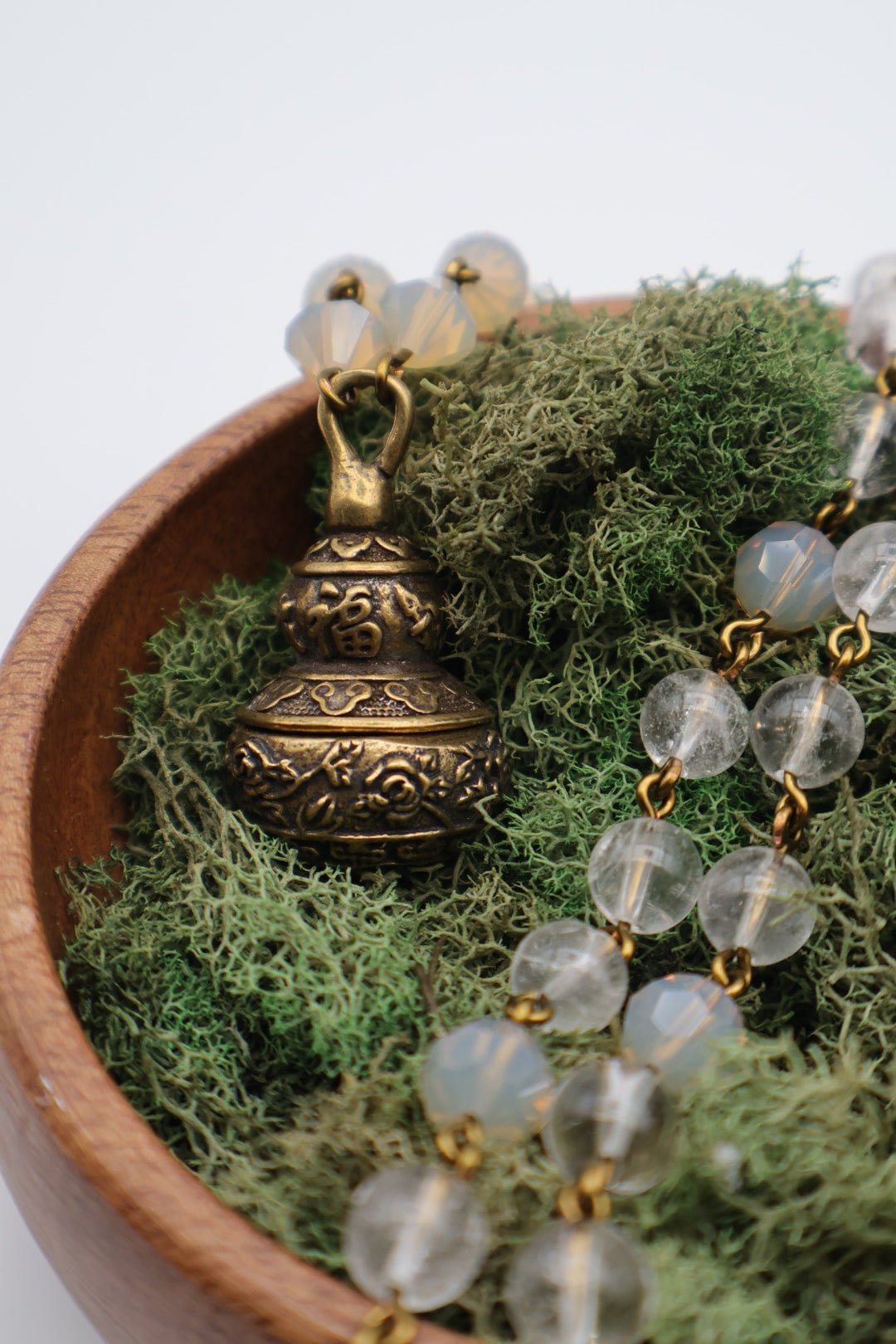 Brass beaded necklace with clear beads on a bed of green moss in a wooden bowl.