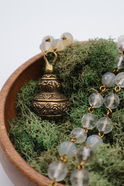 Brass beaded necklace with clear beads on a bed of green moss in a wooden bowl.