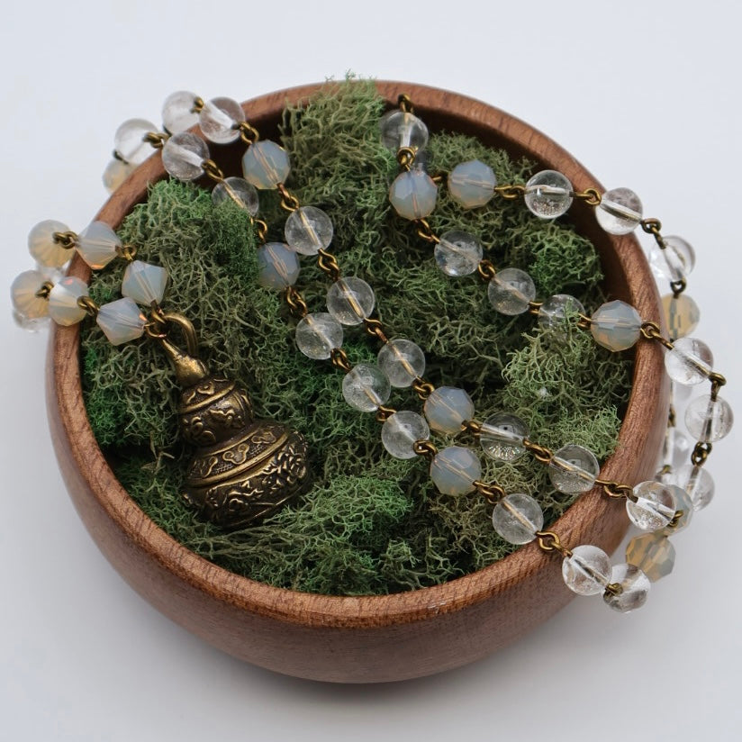 Decorative necklace with clear beads and a bronze pendant on a bed of green moss in a wooden bowl.