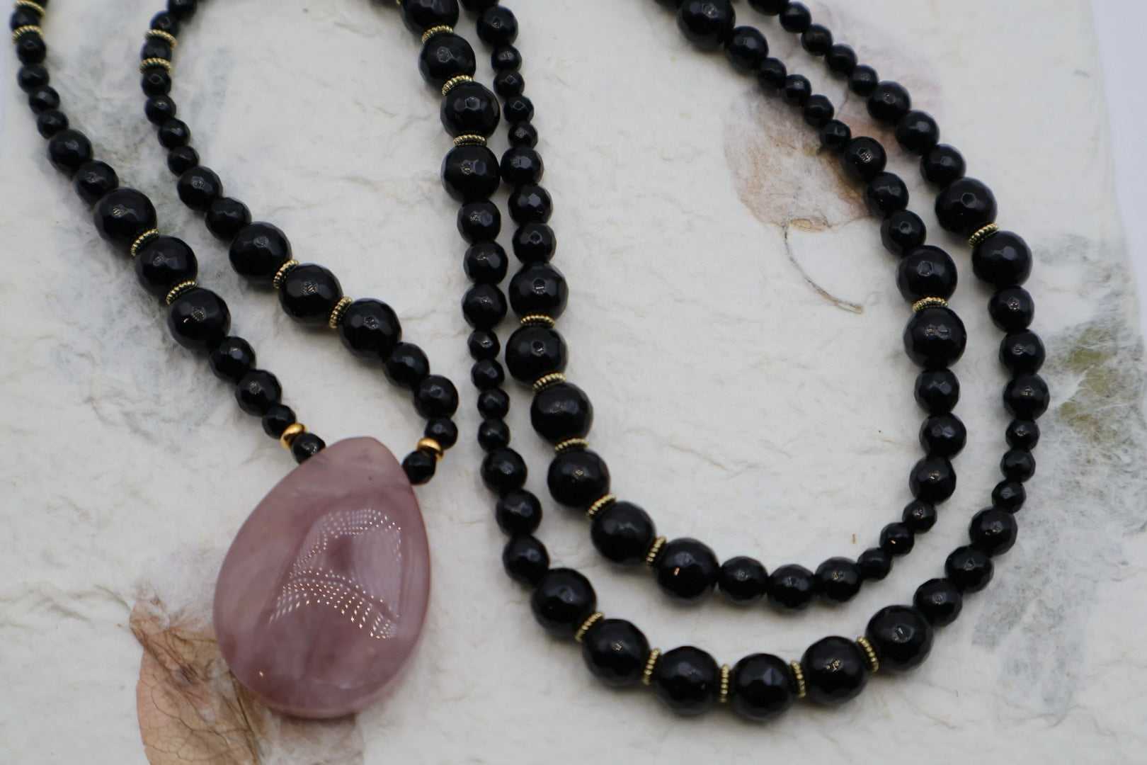Black beaded necklace with a purple stone pendant on a marble surface