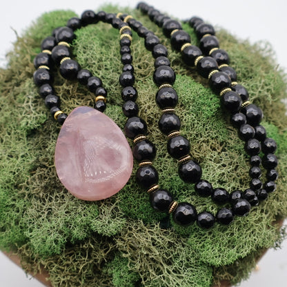 Black beaded necklace with a pink stone pendant on green moss