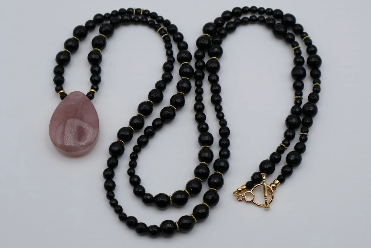 Two black beaded necklaces with a pink stone and gold clasp on a white background