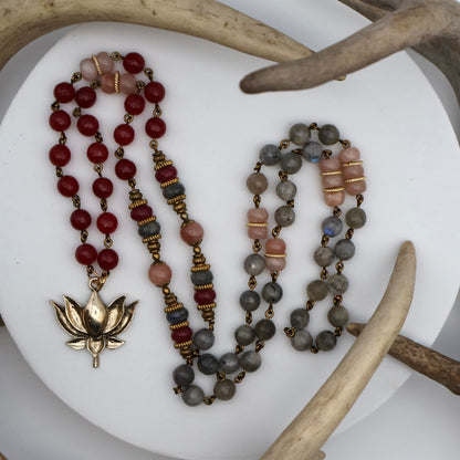 Three beaded necklaces with a gold lotus pendant on a white surface with antlers.