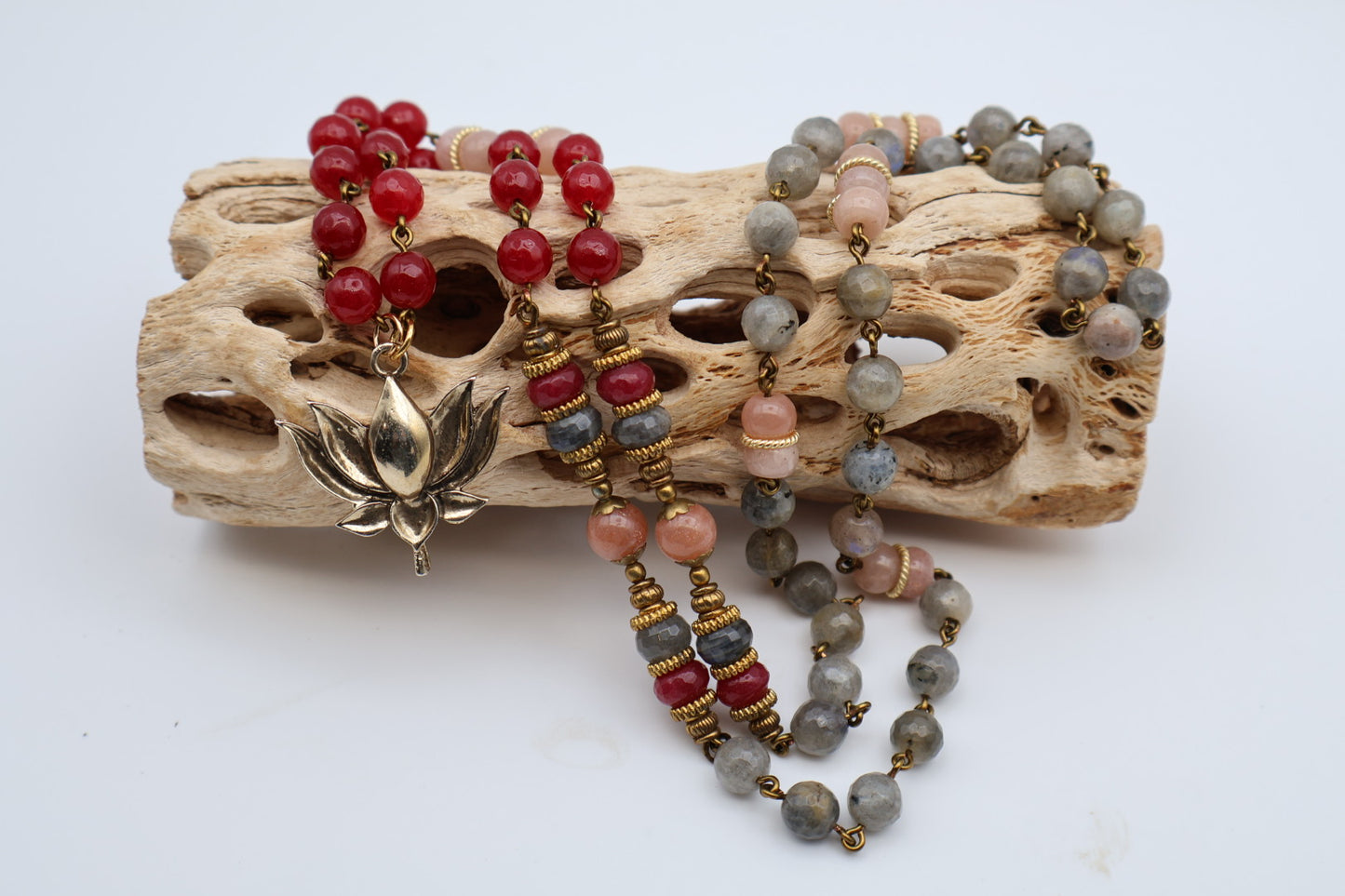 Three beaded necklaces on a piece of driftwood with a white background