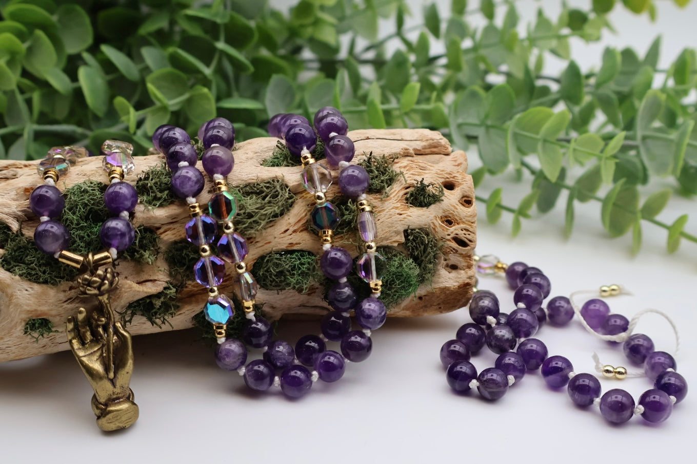 Purple beaded jewelry set with gold accents on a piece of wood and green leaves in the background