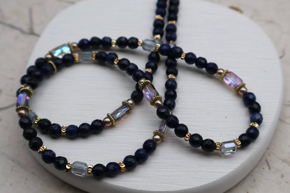 Navy blue beaded necklace with gold and clear accents on a white surface