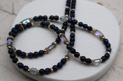 Navy blue beaded necklace with gold and clear accents on a white surface