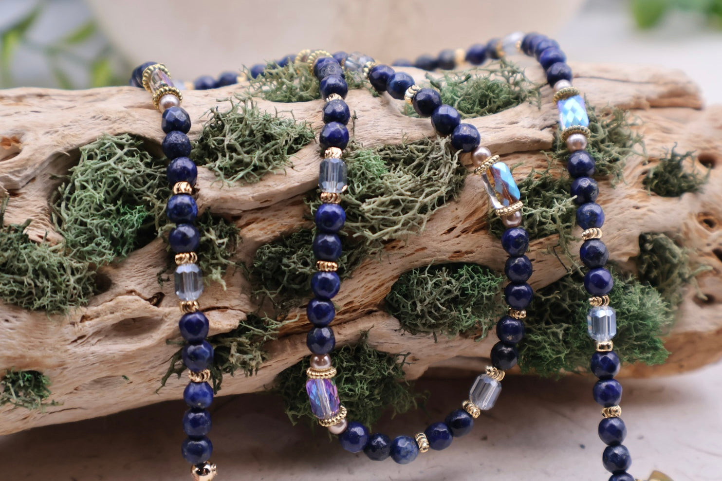 Set of blue beaded bracelets on a piece of driftwood with green moss.