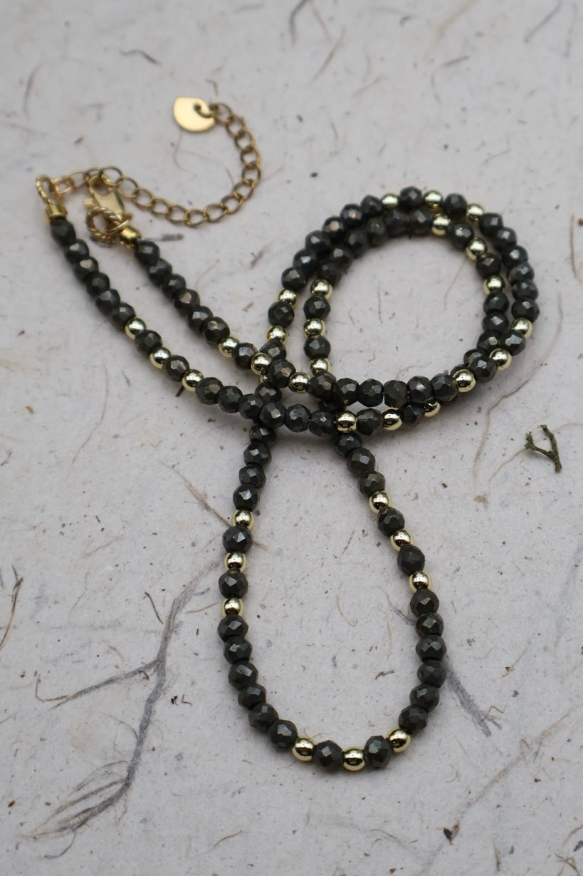 Black beaded necklace with gold accents on a textured surface