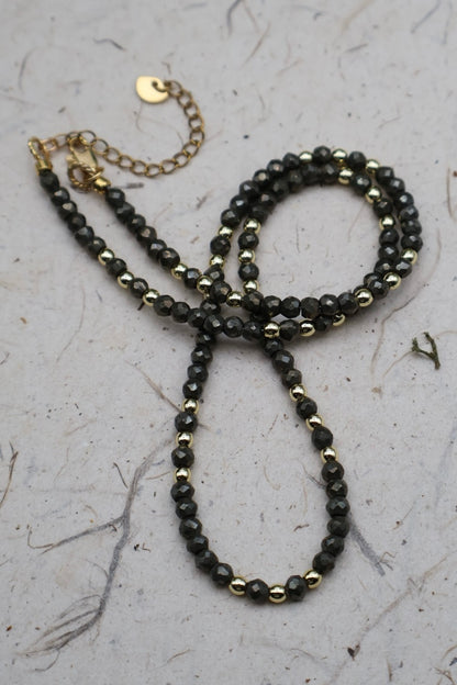 Black beaded necklace with gold accents on a textured surface