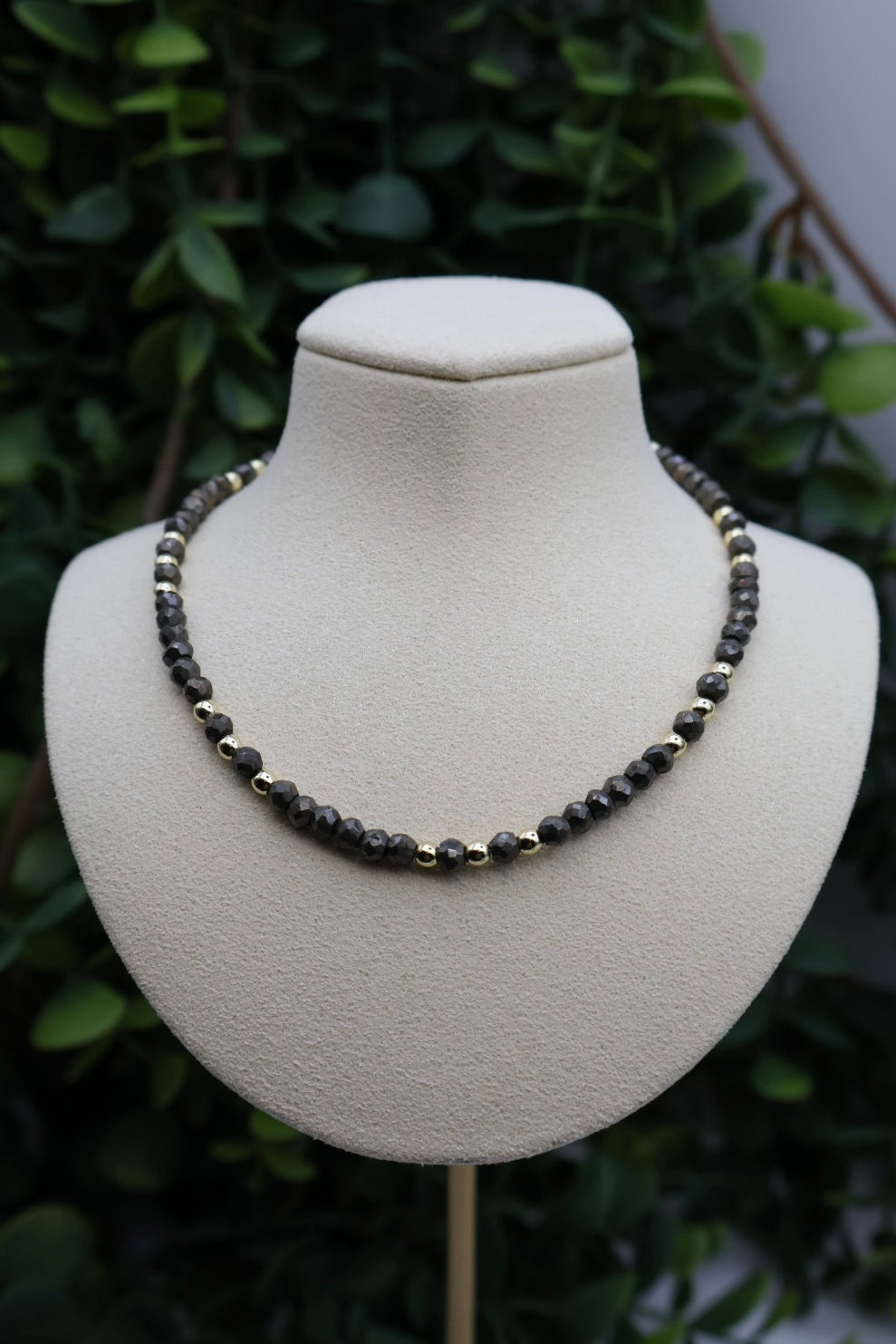 Necklace on a mannequin bust with a green leafy background