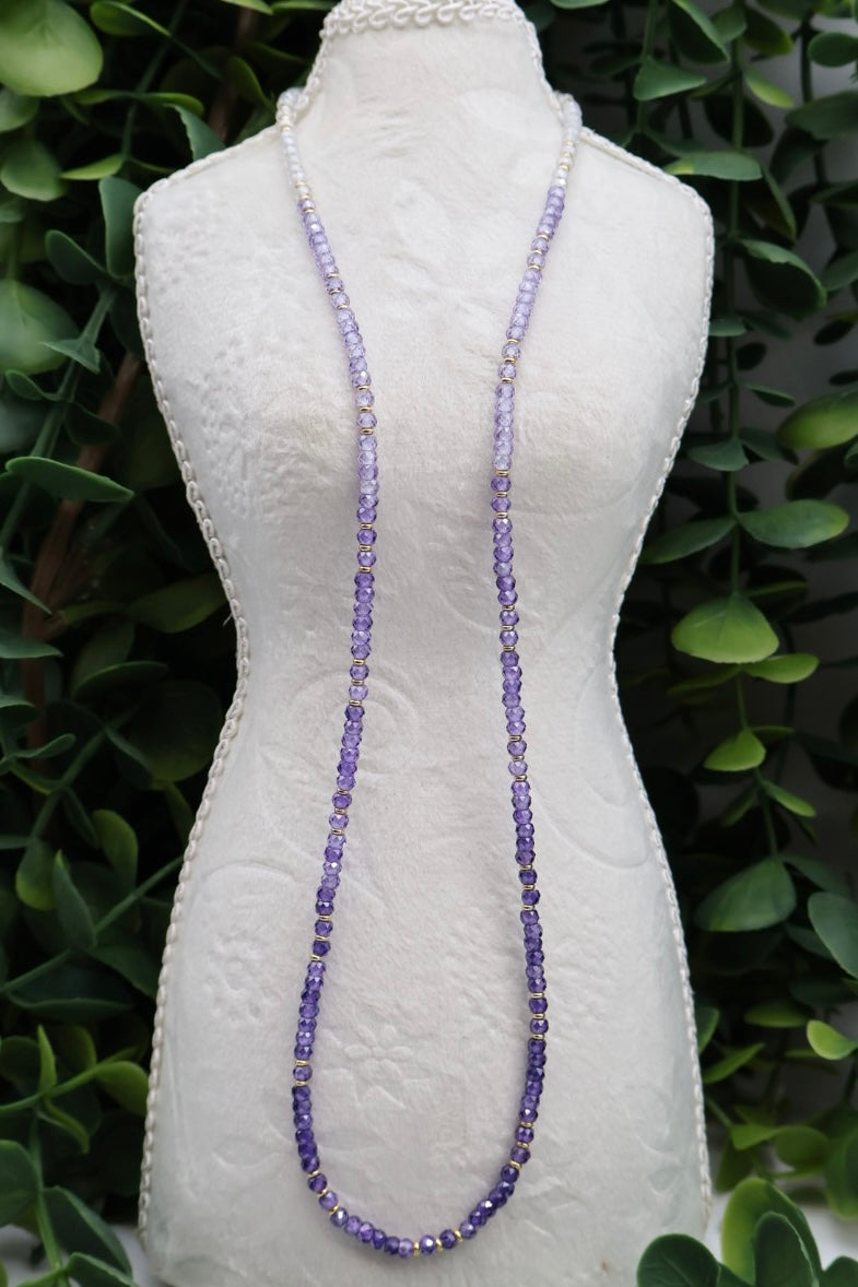 Long beaded necklace on a mannequin against a green leafy background