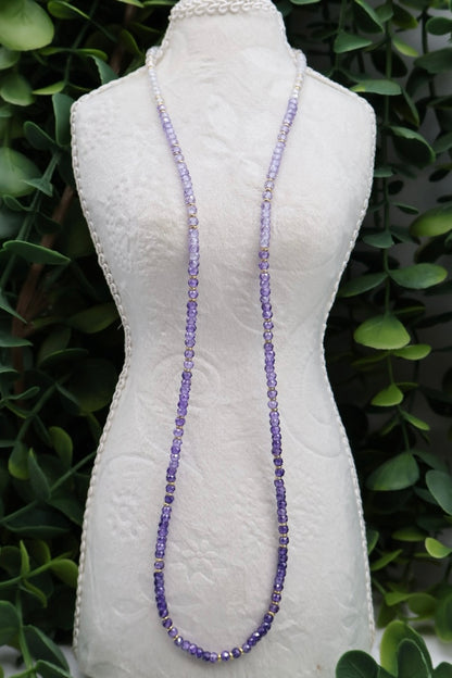 Long beaded necklace on a mannequin against a green leafy background