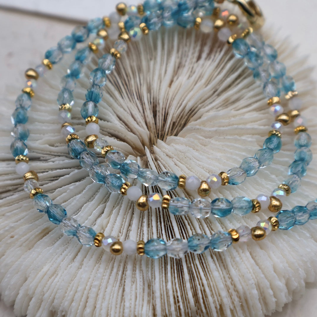 Beaded bracelets with blue, gold, and white beads on a seashell background