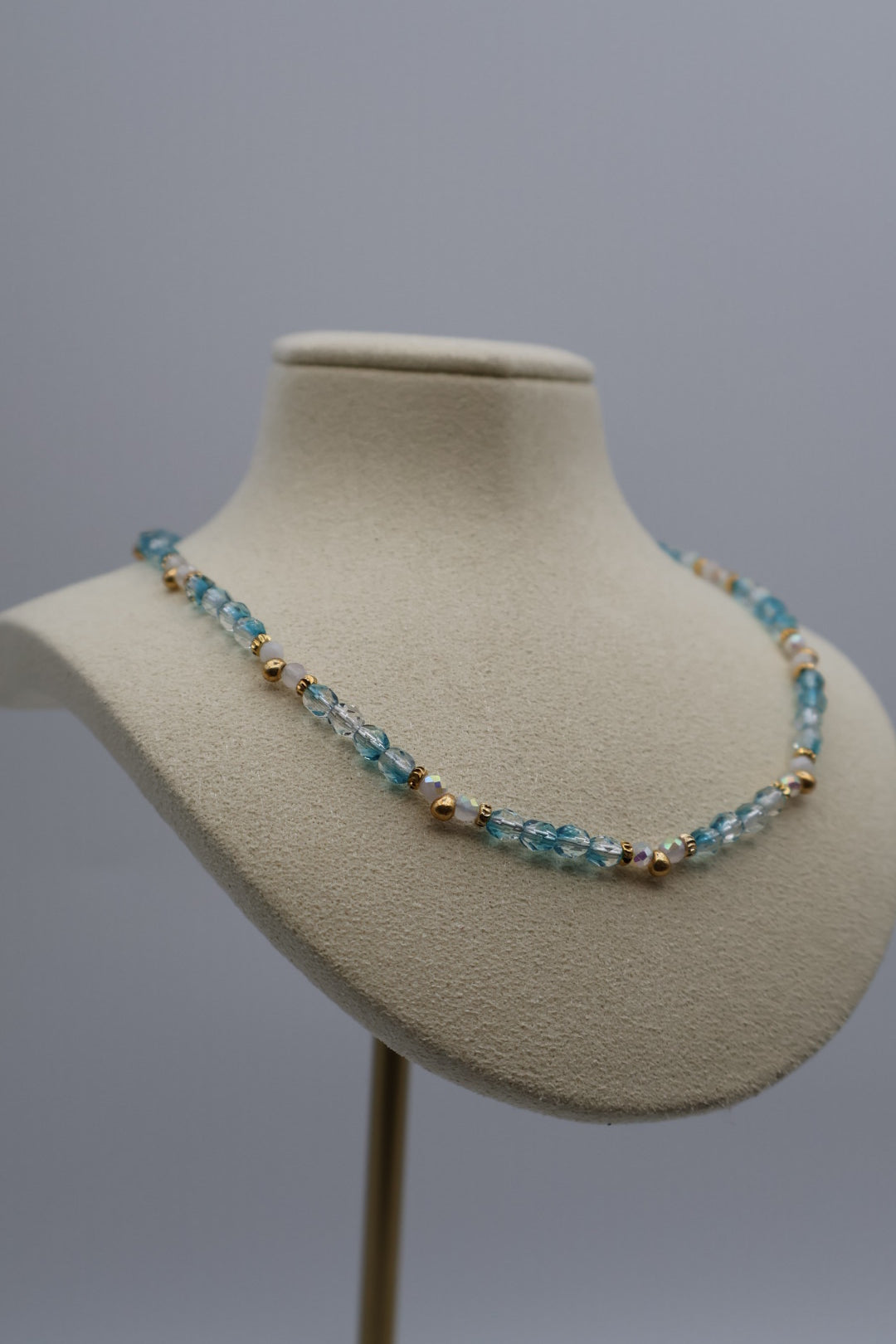 Necklace with blue and gold beads on a mannequin bust against a gray background